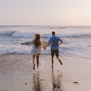 A couple holding hands running into crashing waves along the beach