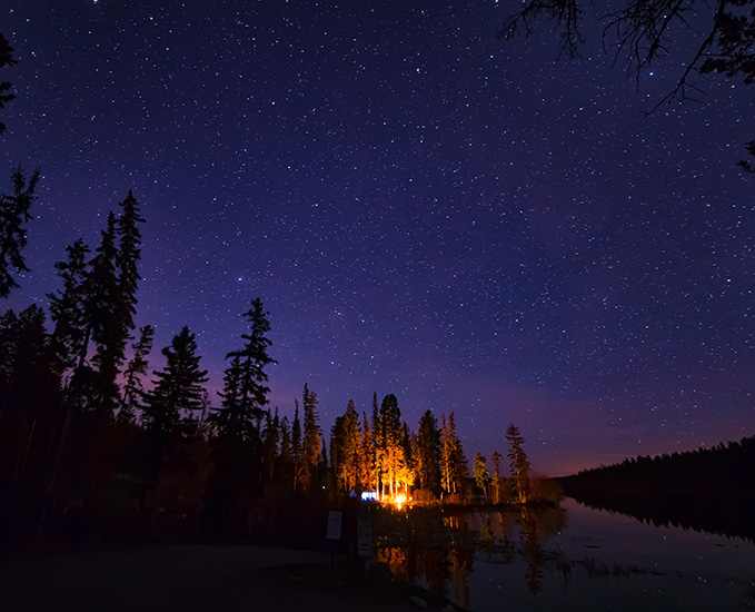 A campfire lights up a night sky filled with stars.