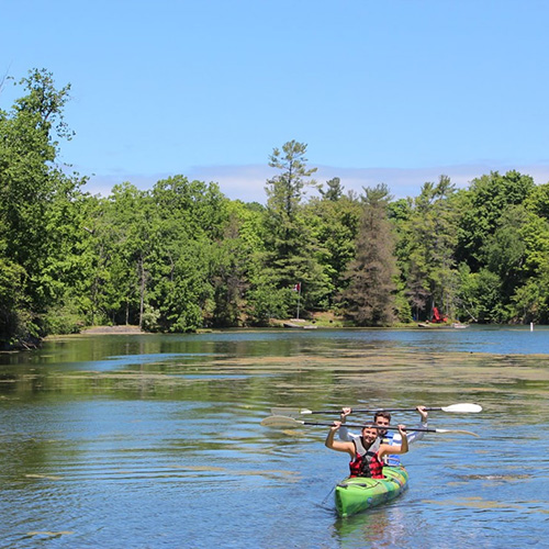Two kayakers hold up their paddles and smile as they make their way through a river.